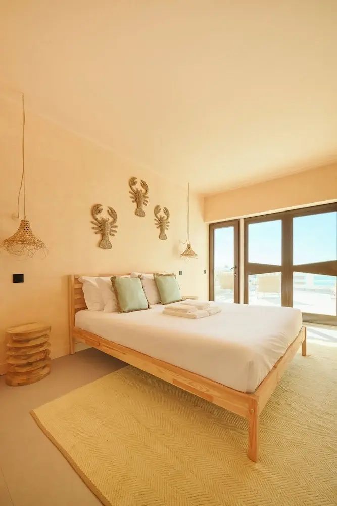 Helles Hotelzimmer mit Holzbett, weißer Bettwäsche, Kissen in Mintgrün und dekorativen Krebsen an der Wand.
