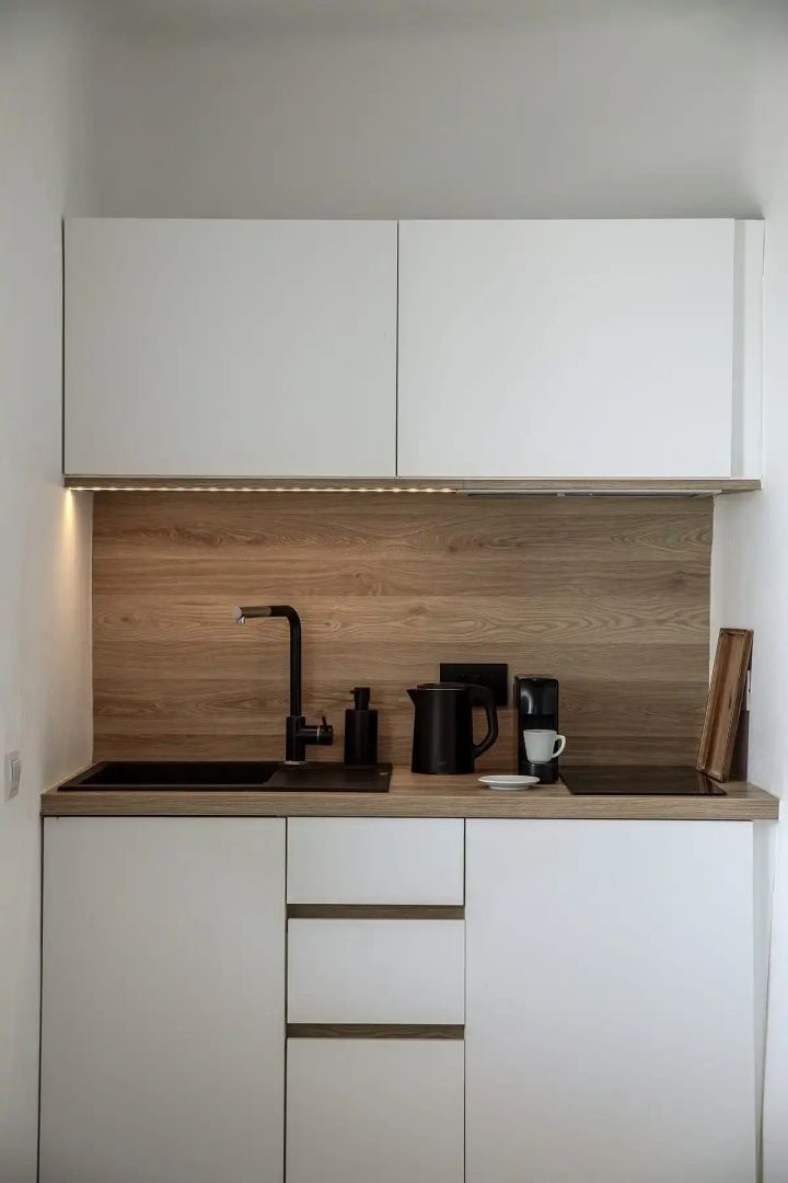 Moderne Küchenzeile in der Suite mit weißen Schränken, Holzrückwand und Kaffeemaschine.