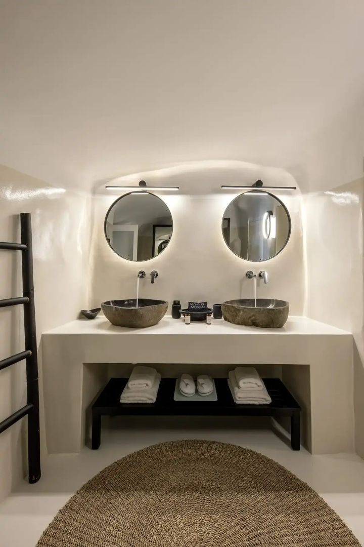 Badezimmer mit zwei Steinwaschbecken auf weißem Waschtisch und zwei beleuchteten Spiegeln.