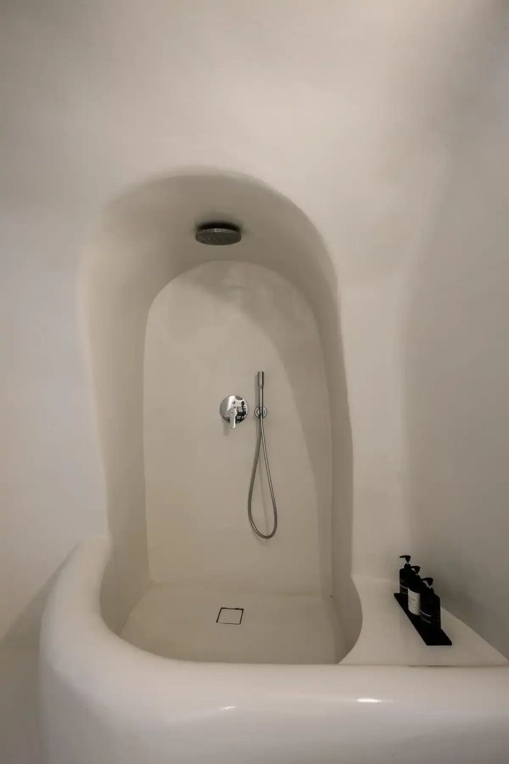 Eine weiße Duschnische im typischen Höhlenstil mit Regenduschkopf und Handbrause.