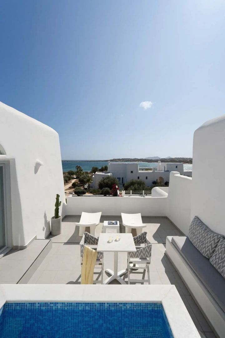 Weiß gestaltete Terrasse mit Sitzgelegenheiten, Sonnenliegen und Blick auf das Meer.