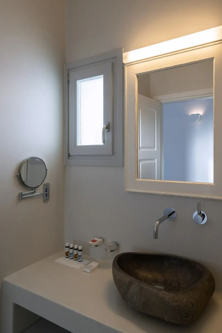 Waschplatz im Badezimmer mit Steinwaschbecken, Spiegel und Pflegeprodukten.