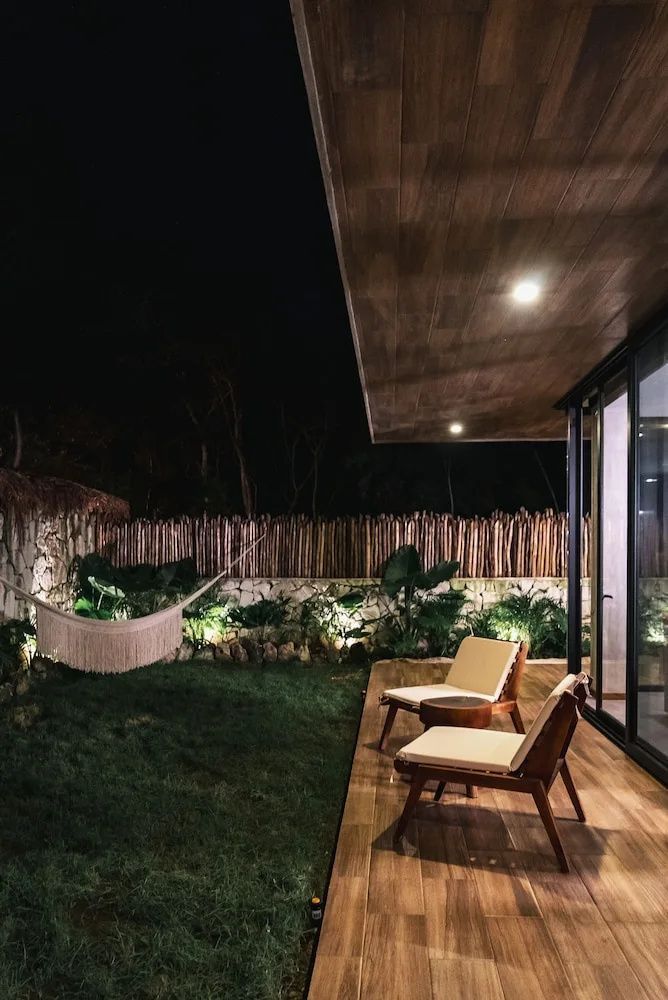 Beleuchtete Terrasse bei Nacht mit zwei Holzsesseln, Rasenfläche und einer Hängematte.
