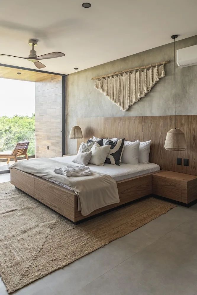 Modernes Hotelzimmer mit großem Holzbett, Makramee-Wandschmuck und Zugang zum Balkon mit Blick ins Grüne.