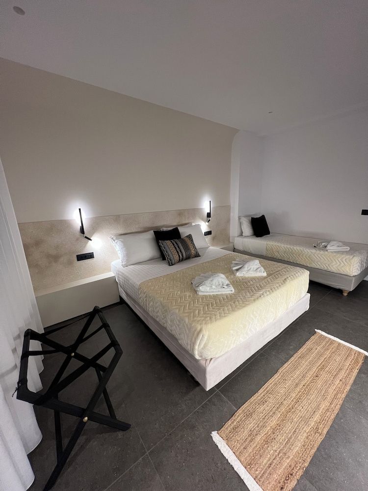 Helles Schlafzimmer mit beigem Kopfteil, Doppelbett, Einzelbett und Läufer auf dem Boden.