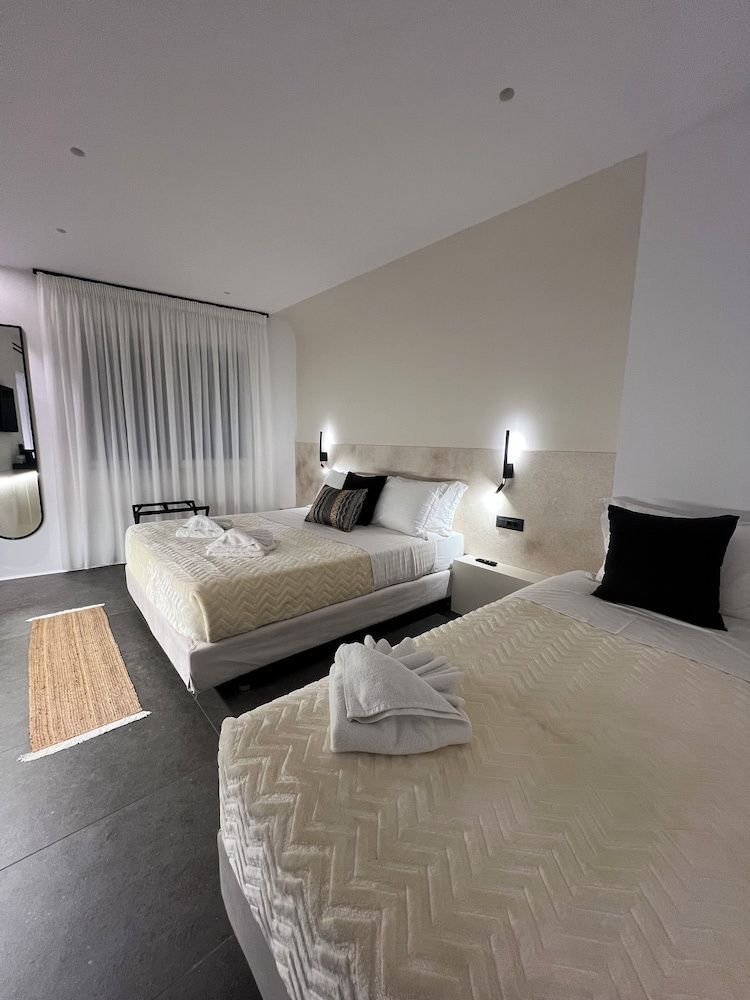Schlafzimmer mit Doppelbett, Vorhängen am Fenster, Wandspiegel und Bett im Vordergrund.