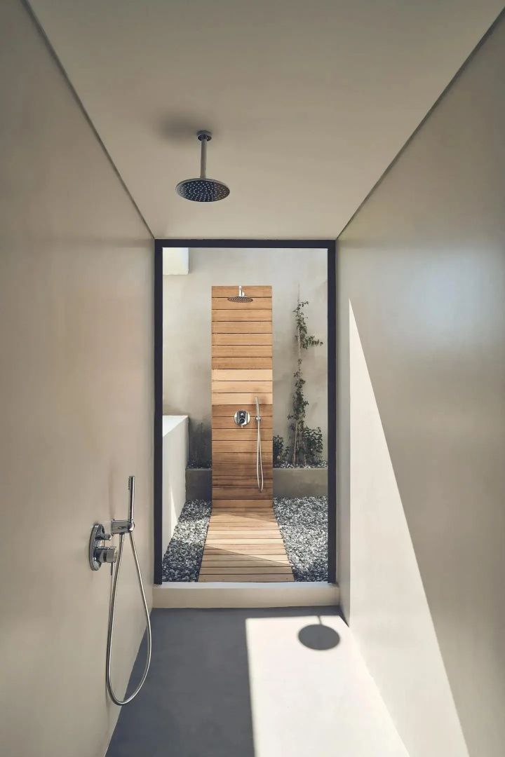 Badezimmer mit Übergang zu einer Außendusche mit Holzelementen und Kieselsteinen.
