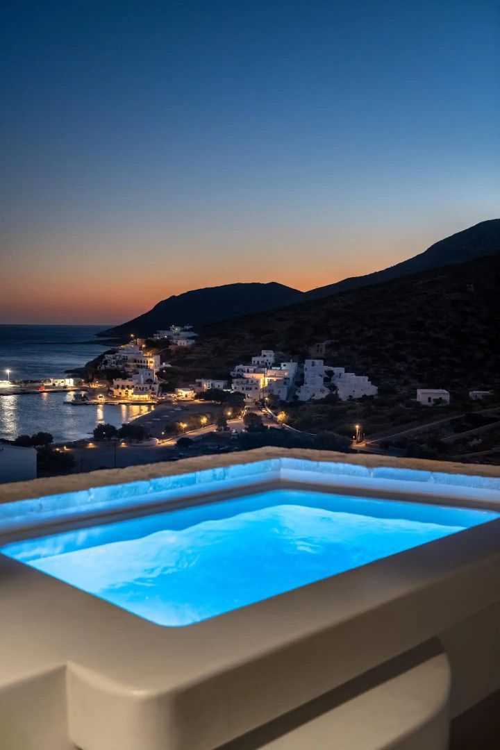 Beleuchtetes Außenbecken am Abend mit Weitblick auf ein beleuchtetes Küstendorf und das Meer.