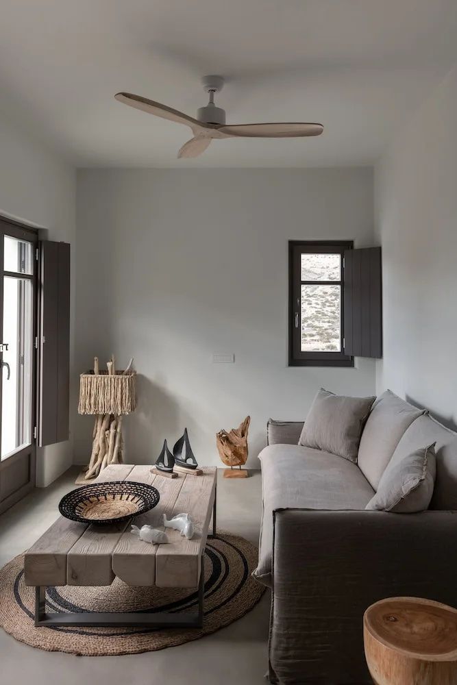 Gemütliche Sitzecke mit grauem Sofa, Holztisch, kleinen Holzbooten und Fensterläden.