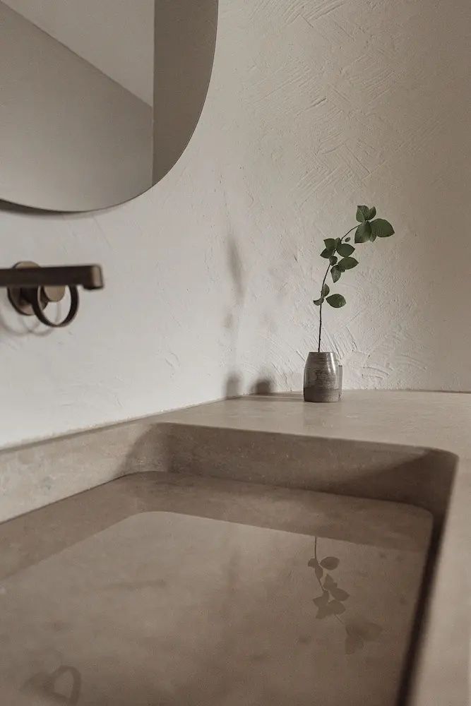 Waschtisch aus Naturstein mit Armatur an einer verputzten Wand und einer Pflanze im Glas.