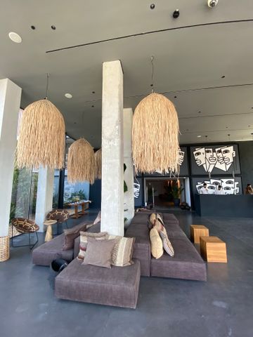 Loungebereich mit großen Strohlampen, braunen Sitzpolstern und betonierten Säulen.