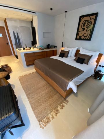 Schlafbereich mit großem Doppelbett, brauner Tagesdecke, Naturteppich und Holzmöbeln.