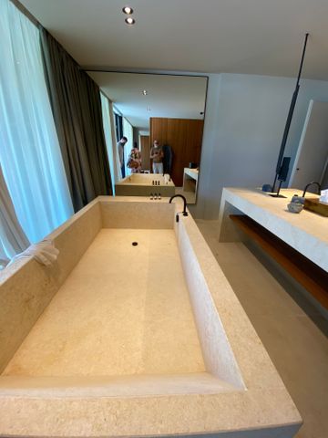 Geräumiges Badezimmer mit großer rechteckiger Steinbadewanne und hellem Waschtisch.