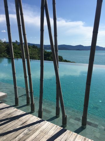 Swimmingpool mit aufrechten Bamboostangen und Blick auf das blaue Meer.