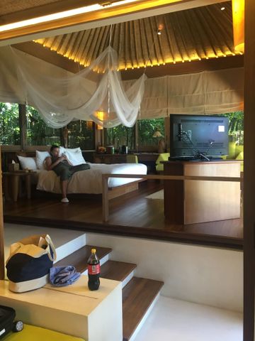 Schlafbereich einer Holzvilla mit Moskitonetz über dem Bett und Fernseher.