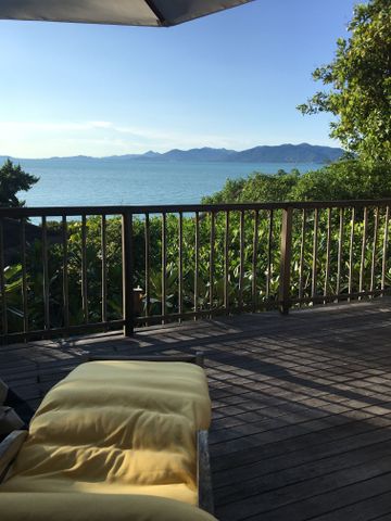 Holzbalkon mit gelb gepolsterter Sonnenliege und Weitblick auf das Meer.