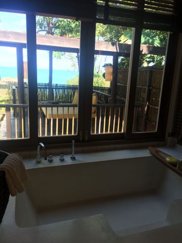 Weiße Badewanne an großen Fenstern mit Blick auf eine Holzterrasse und das Meer.