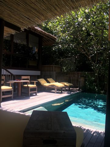 Holzdeck einer Villa mit einem Pool, Liegestühlen und schattenspendenden Bäumen.