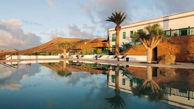 Pool mit Spiegelung von Palmen und weißen Gebäuden vor Vulkanbergen im Hotel César Lanzarote bei Tías