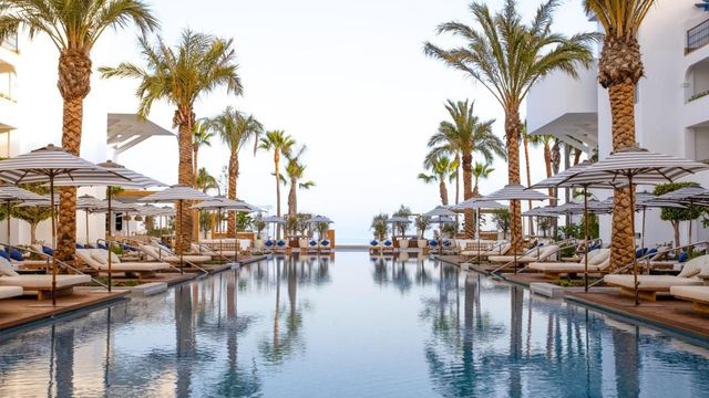 Langer Pool mit Palmen und Sonnenschirmen am Meer im METT Marbella Estepona an der Costa del Sol