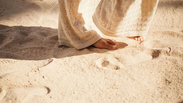 Nackte Füße im Sand unter einem hellen Häkelkleid