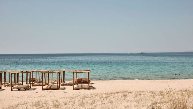 Sandstrand mit Holzpavillons und Liegen am türkisfarbenen Meer