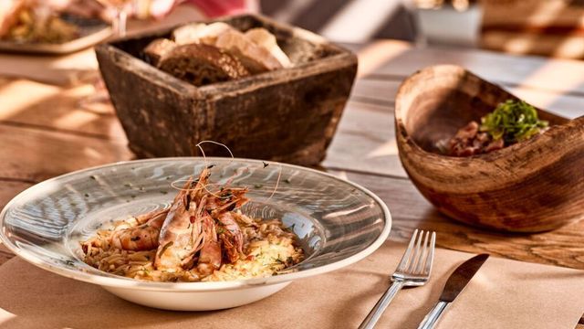 Garnelengericht und Brot in Holzschalen auf einem Restauranttisch in der Sonne